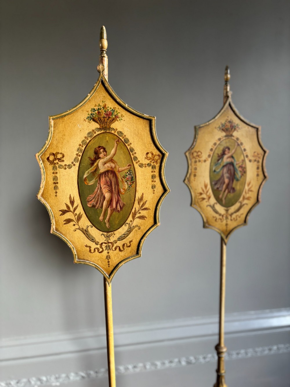 A pair of antique Georgian cream-painted wooden pole screens featuring hand-painted classical figures on shaped panels supported by tripod bases with spade feet. View VIII