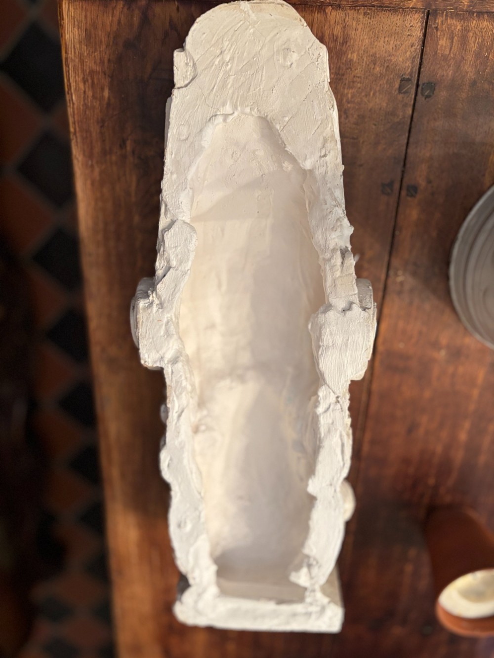 A carved off-white plaster wall corbel featuring a winged putto head above an acanthus leaf support. View XV
