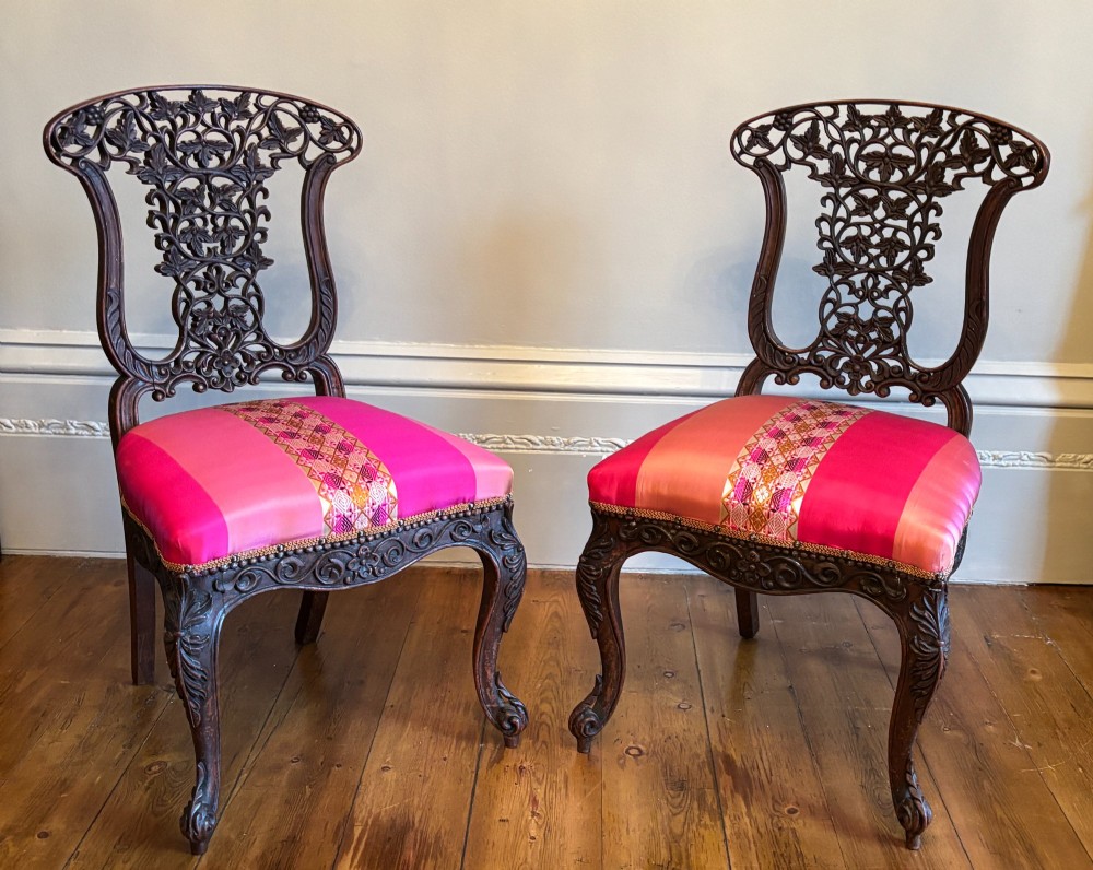 A pair of 19th century Anglo-Indian padauk side chairs with intricately carved openwork foliate backs, cabriole legs, and pink silk upholstery. View V
