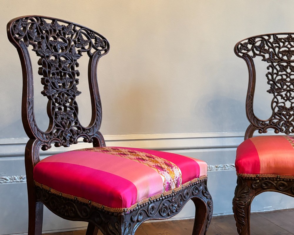 A pair of 19th century Anglo-Indian padauk side chairs with intricately carved openwork foliate backs, cabriole legs, and pink silk upholstery. View VI