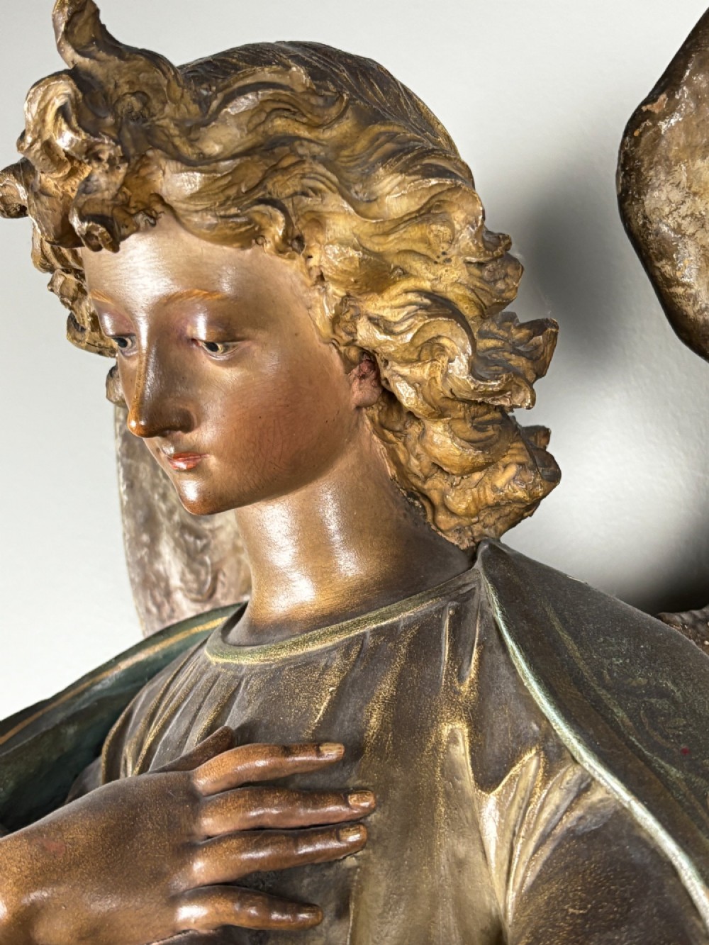 A 19th-century carved Italian wooden angel statue with gold wings, painted drapery in muted blue and ochre tones, and hands resting across its chest. View V