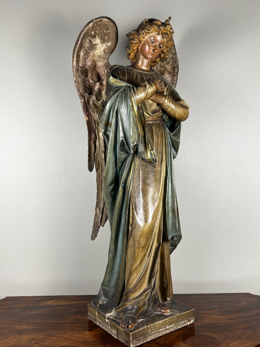 A 19th-century carved Italian wooden angel statue with gold wings, painted drapery in muted blue and ochre tones, and hands resting across its chest. View VI