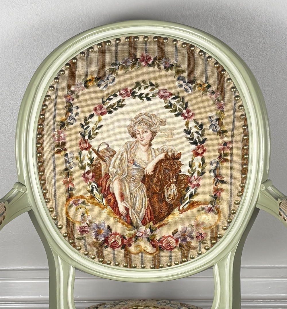 A French Louis XVI style open armchair painted in pale green with an oval backrest and needlepoint tapestry upholstery depicting a figure and floral motifs. View II