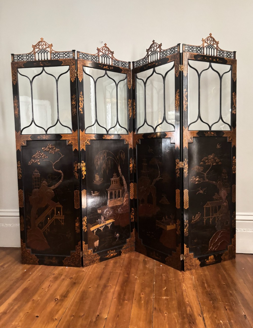 A four-panel black lacquered coromandel screen featuring Chinese Chippendale pagoda crestings, arched glazed tracery windows, and gilt landscape scenes.