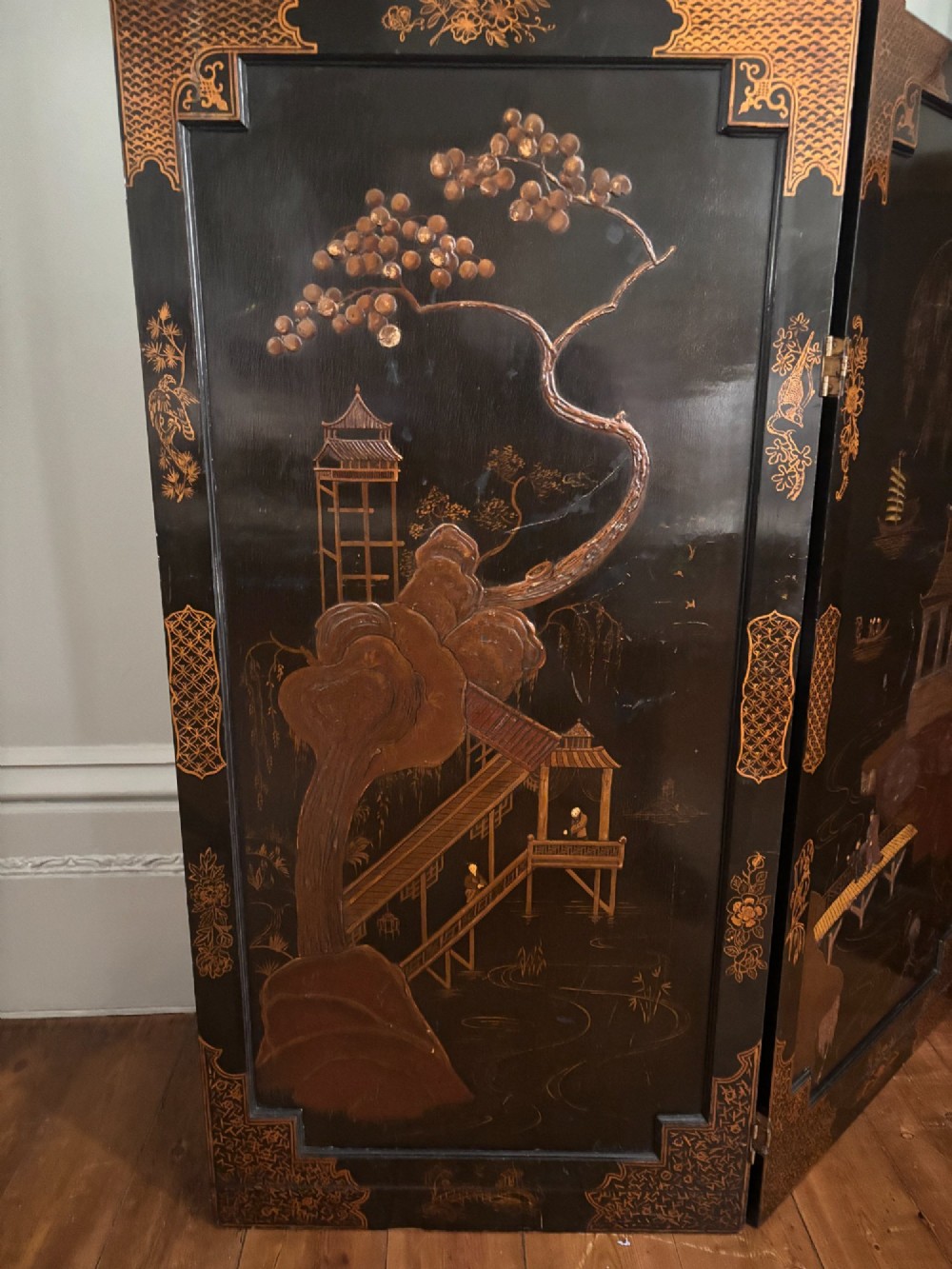 A four-panel black lacquered coromandel screen featuring Chinese Chippendale pagoda crestings, arched glazed tracery windows, and gilt landscape scenes. View V