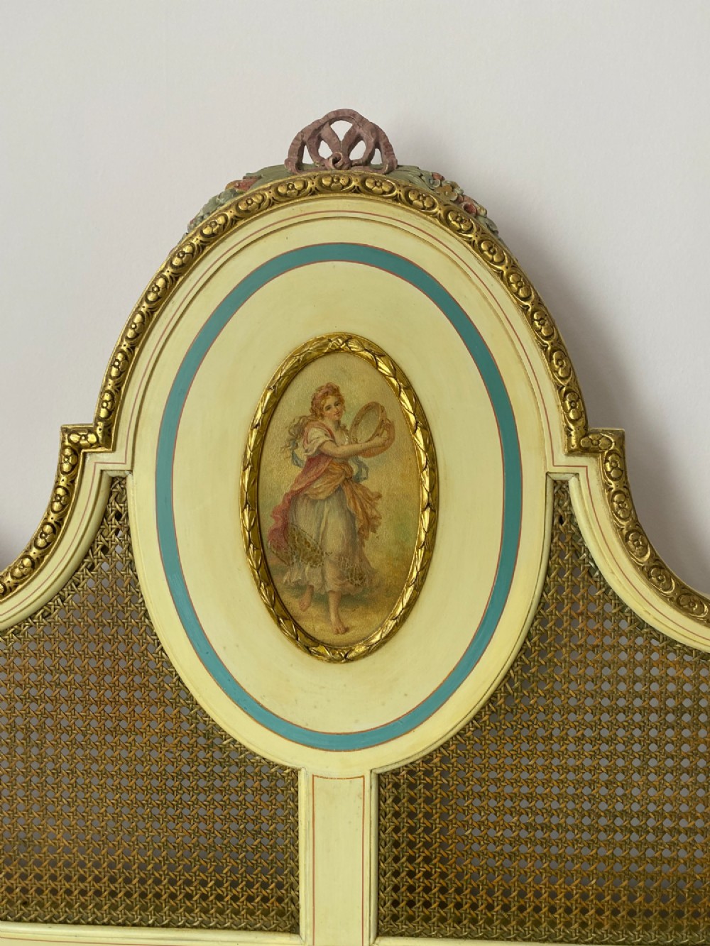 A pair of cream-painted single bedsteads featuring oval hand-painted portrait medallions, woven cane back panels, parcel gilding, and carved paw feet. View V
