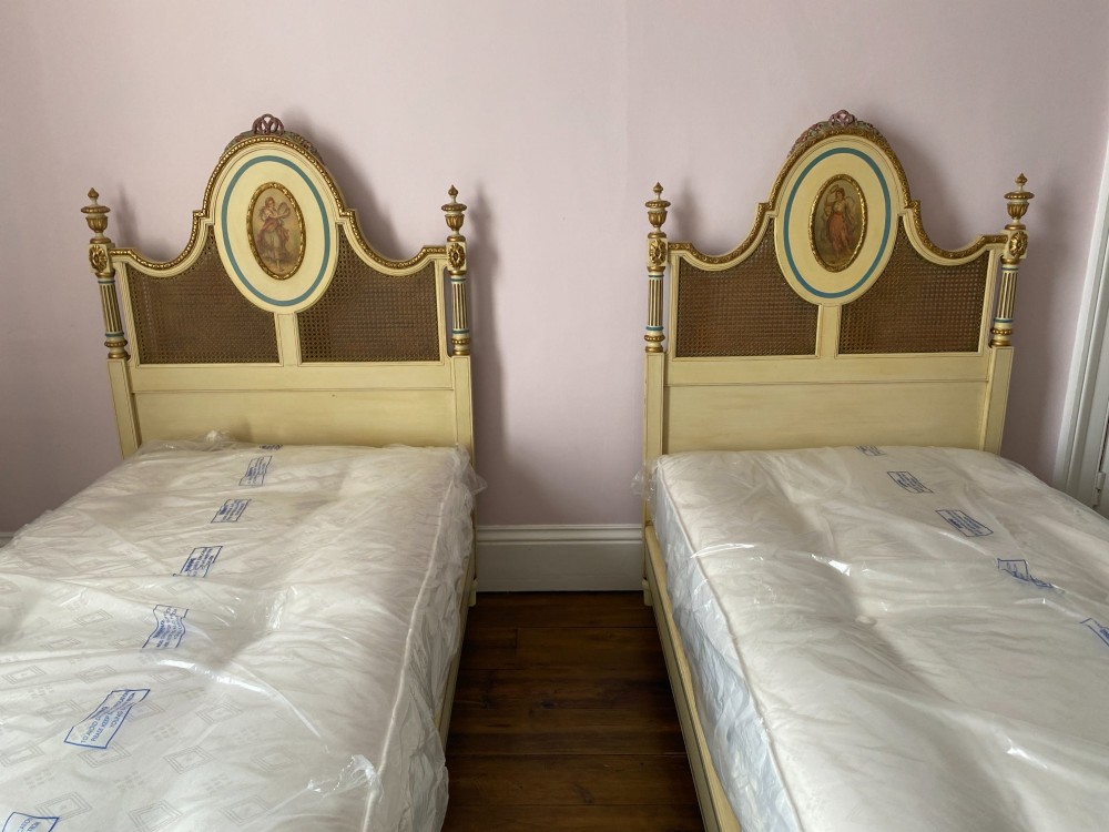 A pair of cream-painted single bedsteads featuring oval hand-painted portrait medallions, woven cane back panels, parcel gilding, and carved paw feet. View XIII
