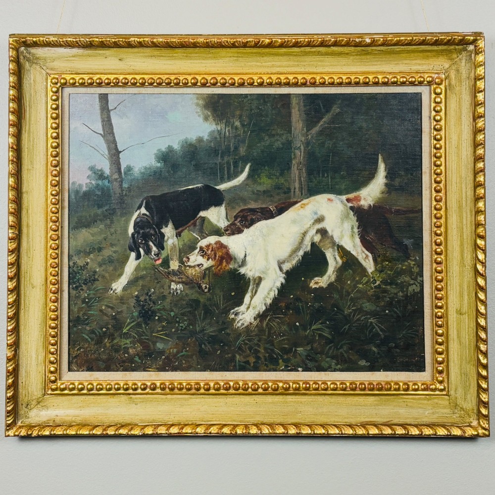 A framed oil painting on canvas depicting hunting dogs retrieving a game bird in a woodland clearing.