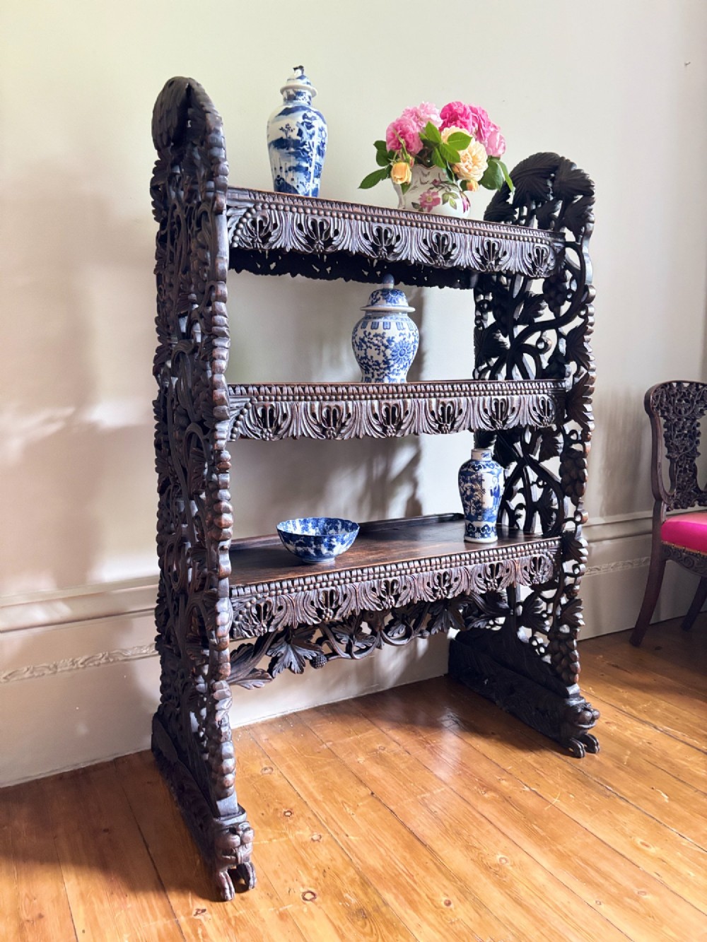 A mid-19th-century Anglo-Indian dark padauk wood open shelving unit with three tiers, intricate foliate carving, pierced aprons, and carved feet. View III