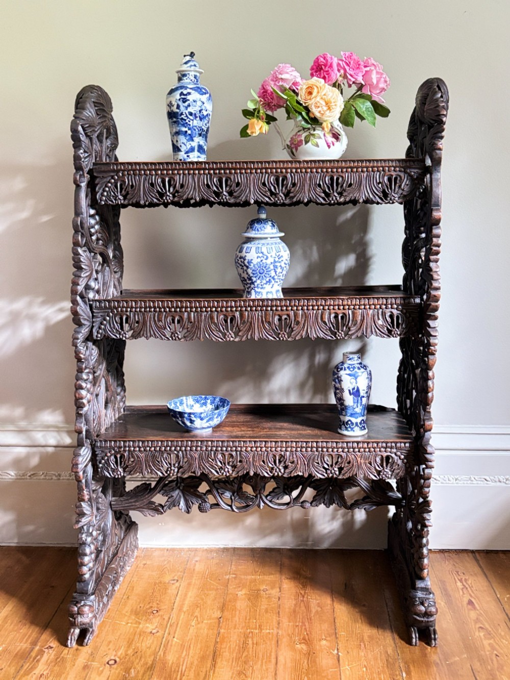 A mid-19th-century Anglo-Indian dark padauk wood open shelving unit with three tiers, intricate foliate carving, pierced aprons, and carved feet. View XI