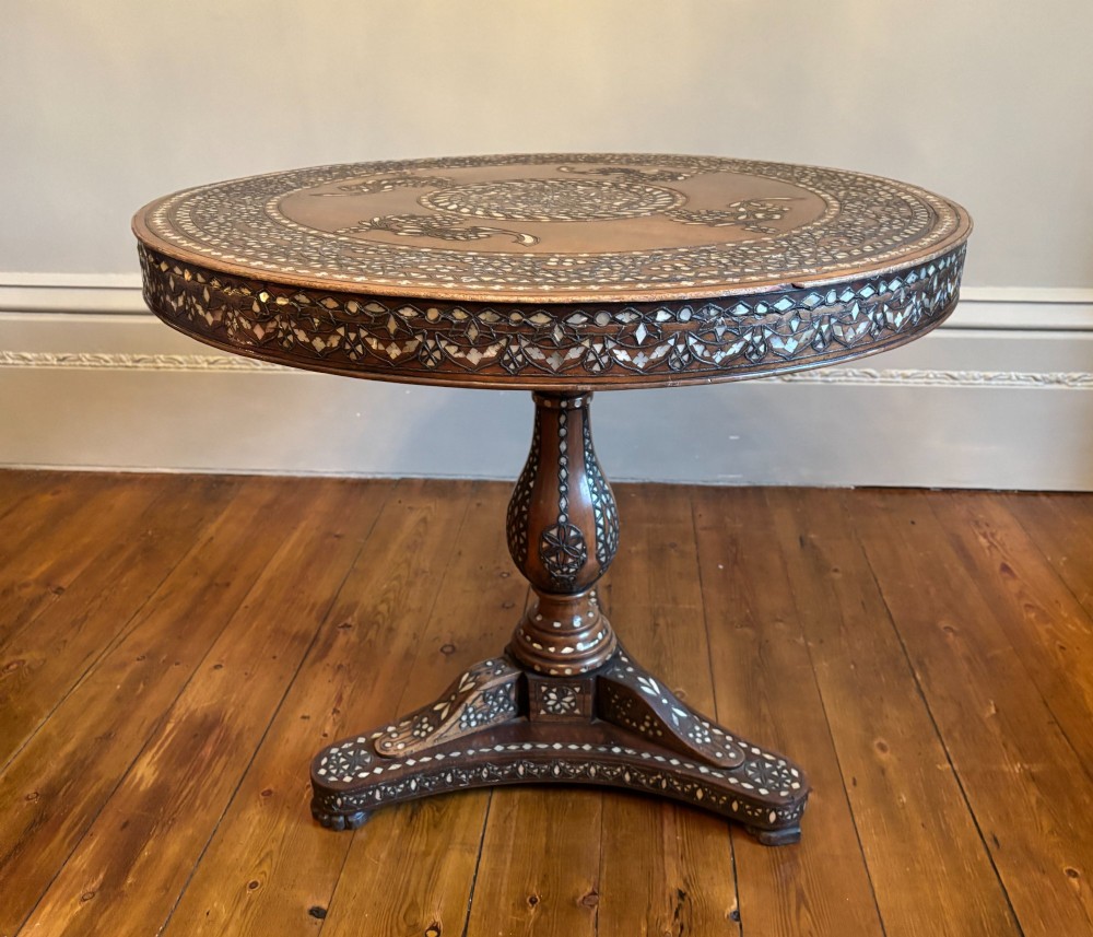 A 19th-century circular Anglo-Indian pedestal table made of dark hardwood with geometric mother-of-pearl inlay across the top, apron, turned column, and tripod base.