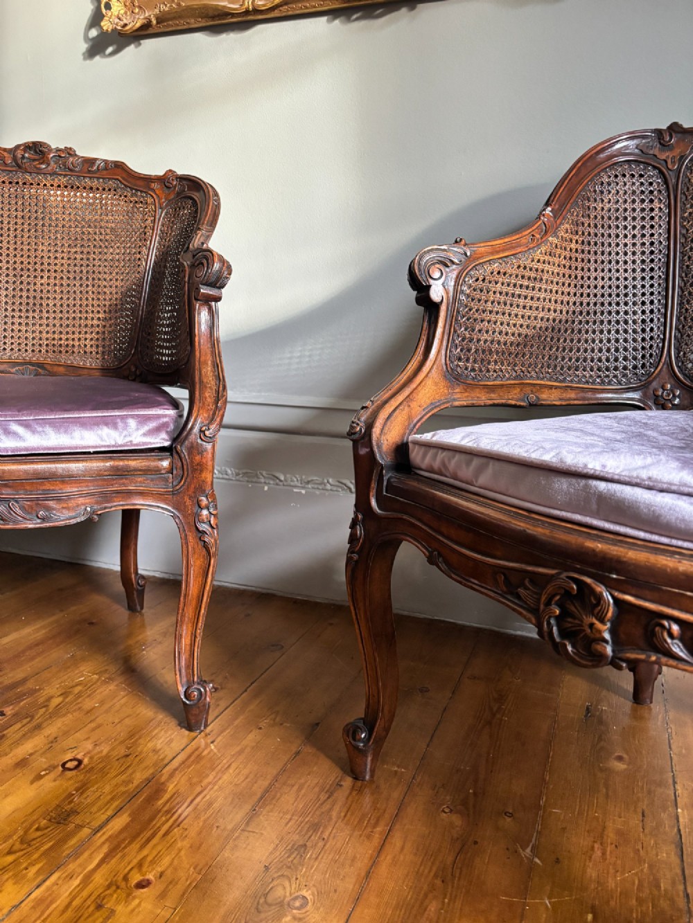 A pair of French Louis XV style carved wooden armchairs with woven cane backrests and purple velvet seat cushions resting on cabriole legs. View IV