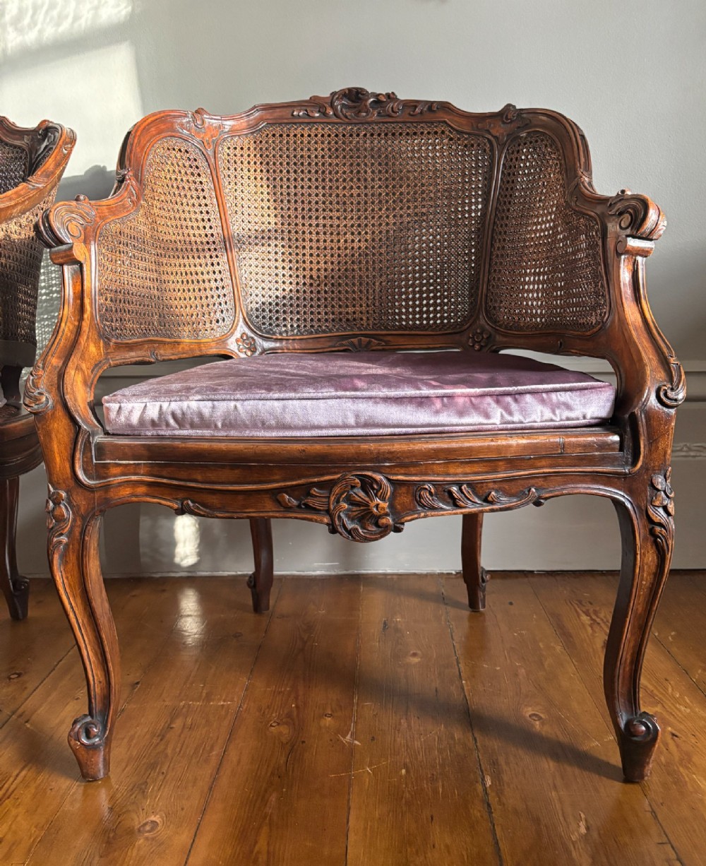 A pair of French Louis XV style carved wooden armchairs with woven cane backrests and purple velvet seat cushions resting on cabriole legs. View VI