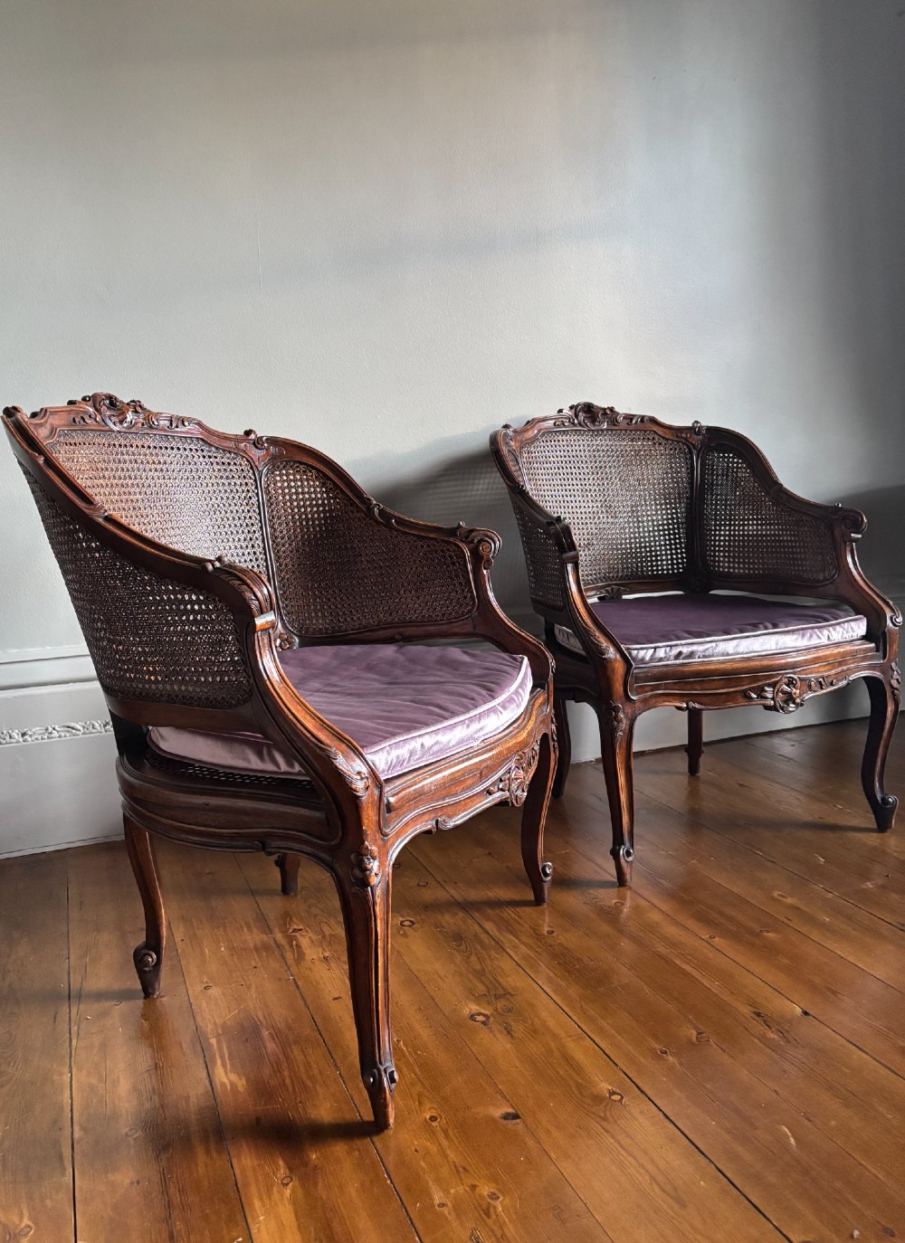 A pair of French Louis XV style carved wooden armchairs with woven cane backrests and purple velvet seat cushions resting on cabriole legs. View X