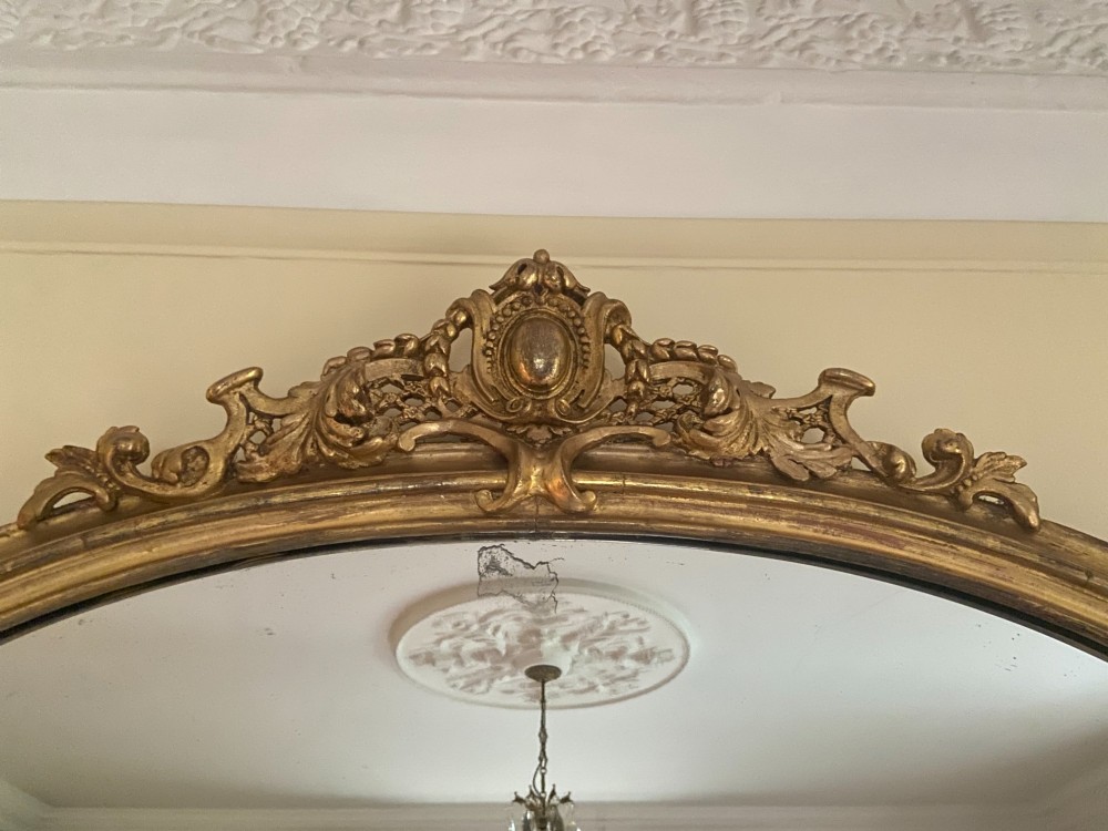A large mid-nineteenth century giltwood overmantel mirror featuring a waisted arched frame, carved pediment cresting, and scroll motifs at the base. View III