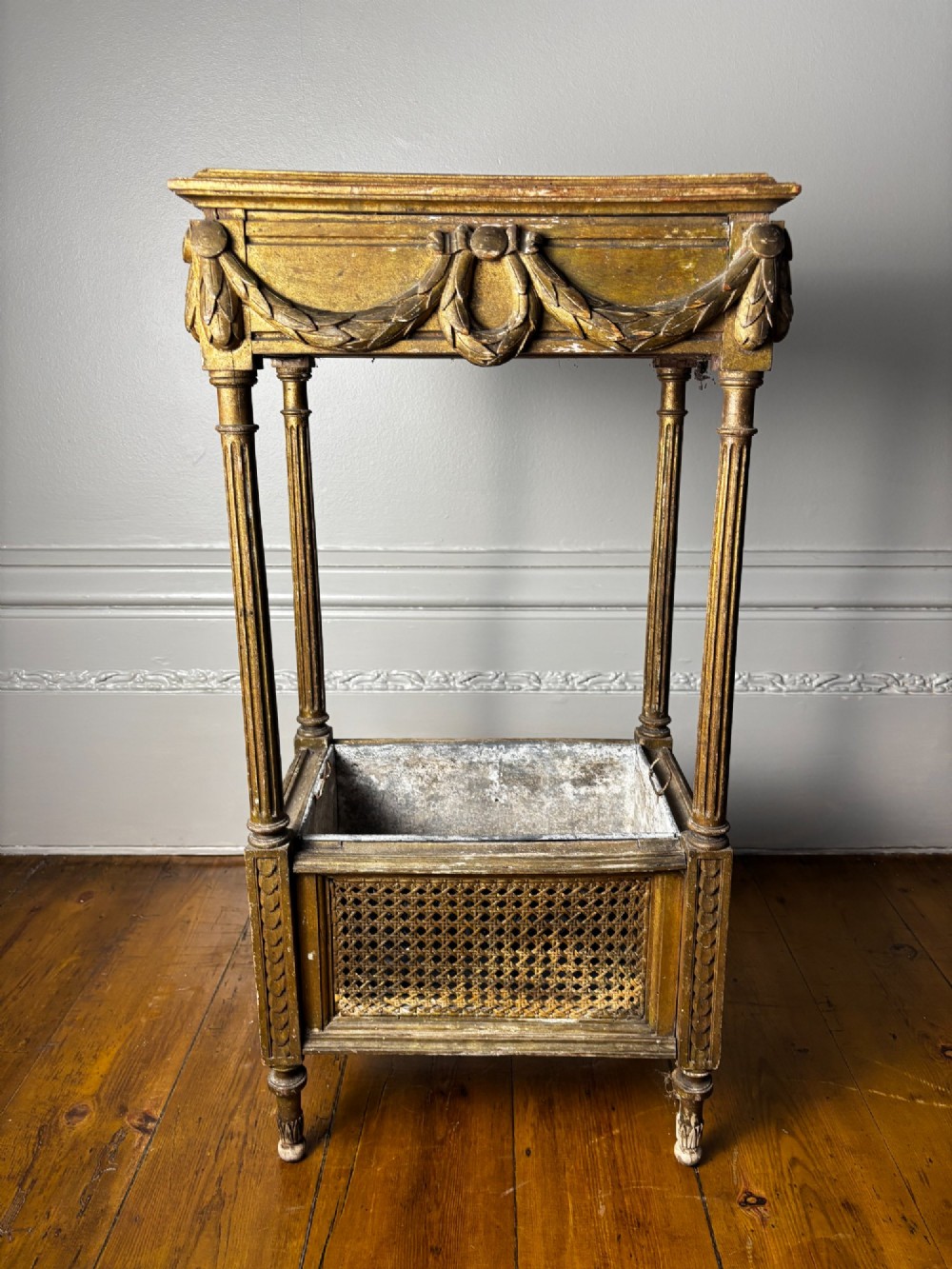 A two-tiered French Empire giltwood jardinere stand featuring carved festoons, fluted supports, and a lower caned trough with a removable metal liner. View II