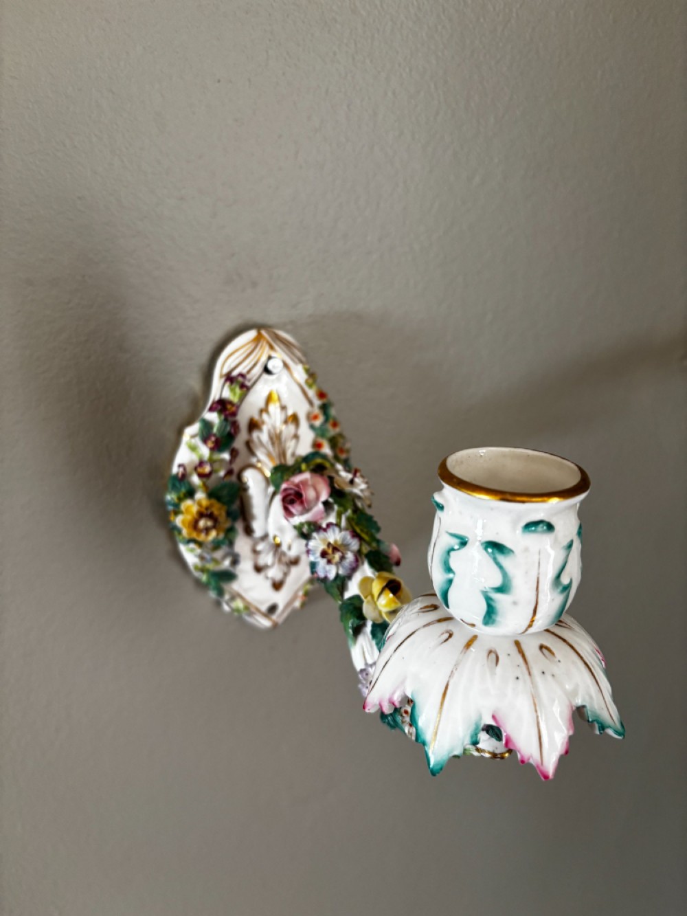 A white porcelain single candle wall sconce with hand-painted applied floral decorations, green foliage, and gilded Rococo scrollwork. View II