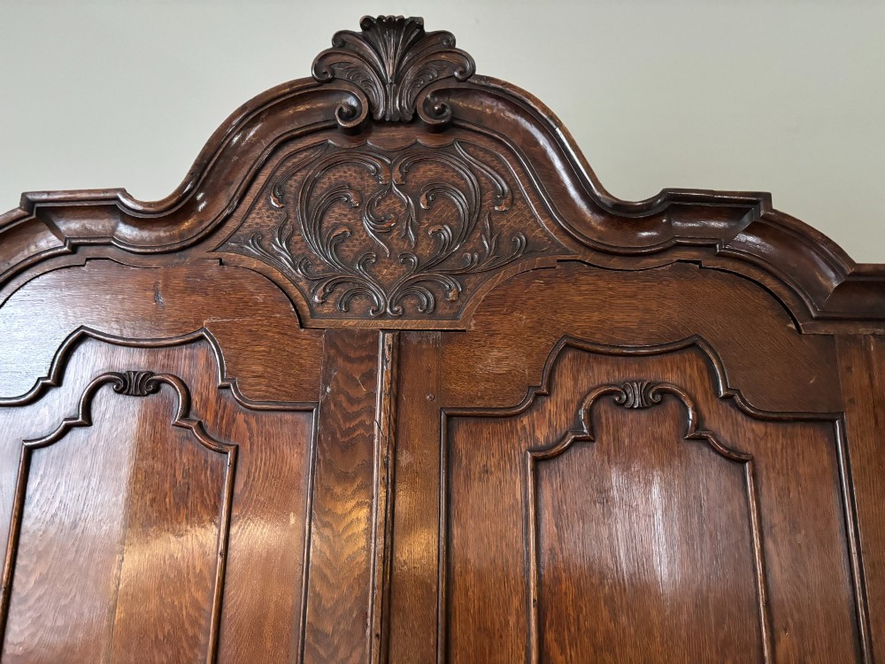 An 18th-century Dutch oak linen press featuring an arched pediment, two carved panel doors, three lower drawers, and brass handles. View III