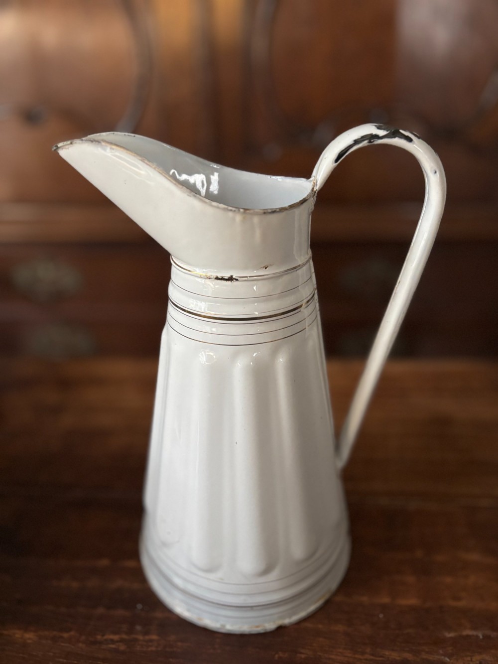 A tall white enamelled metal water jug featuring fluted vertical panels and thin gilt line detailing around the neck and base. View II