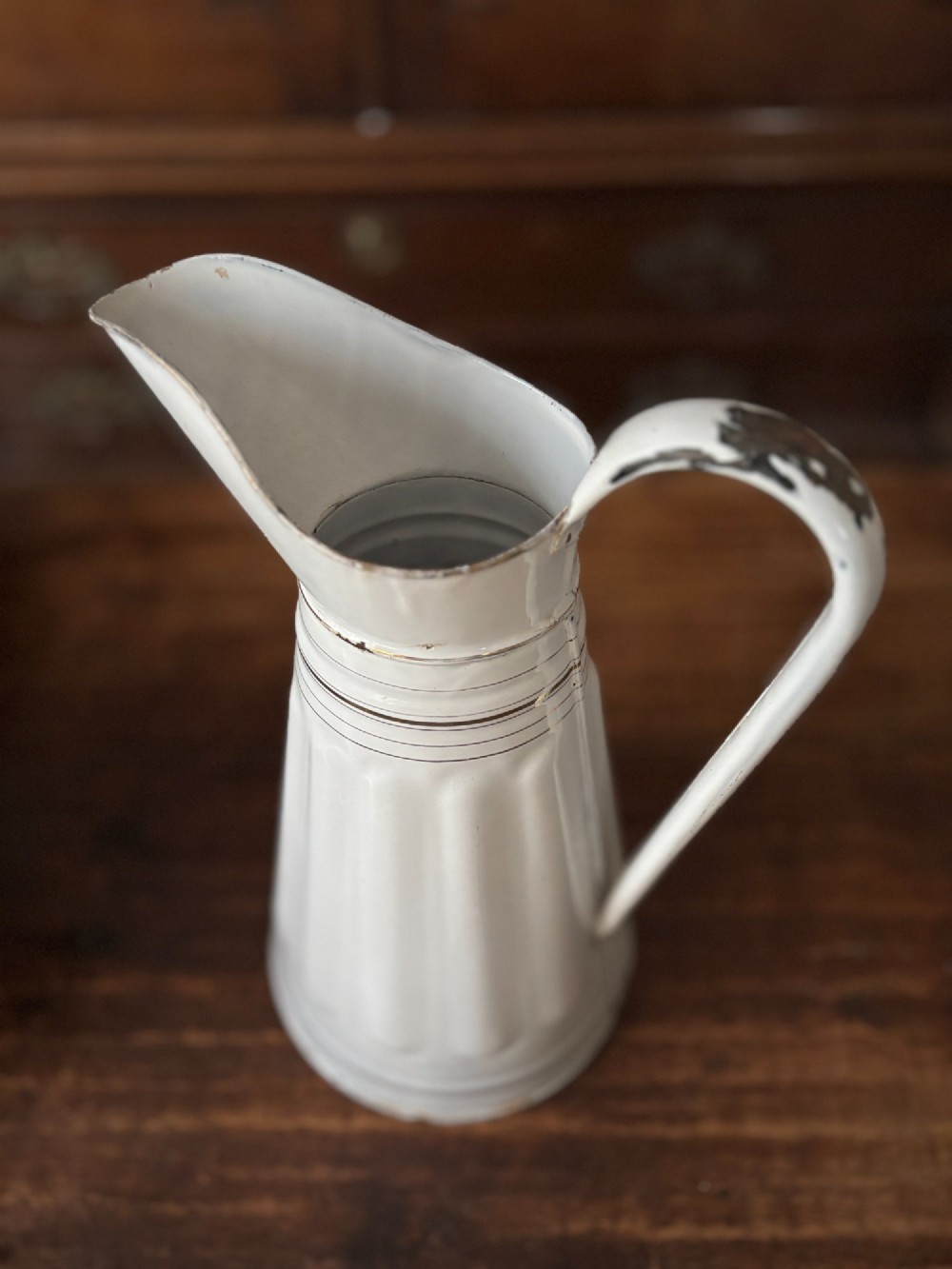 A tall white enamelled metal water jug featuring fluted vertical panels and thin gilt line detailing around the neck and base. View IV