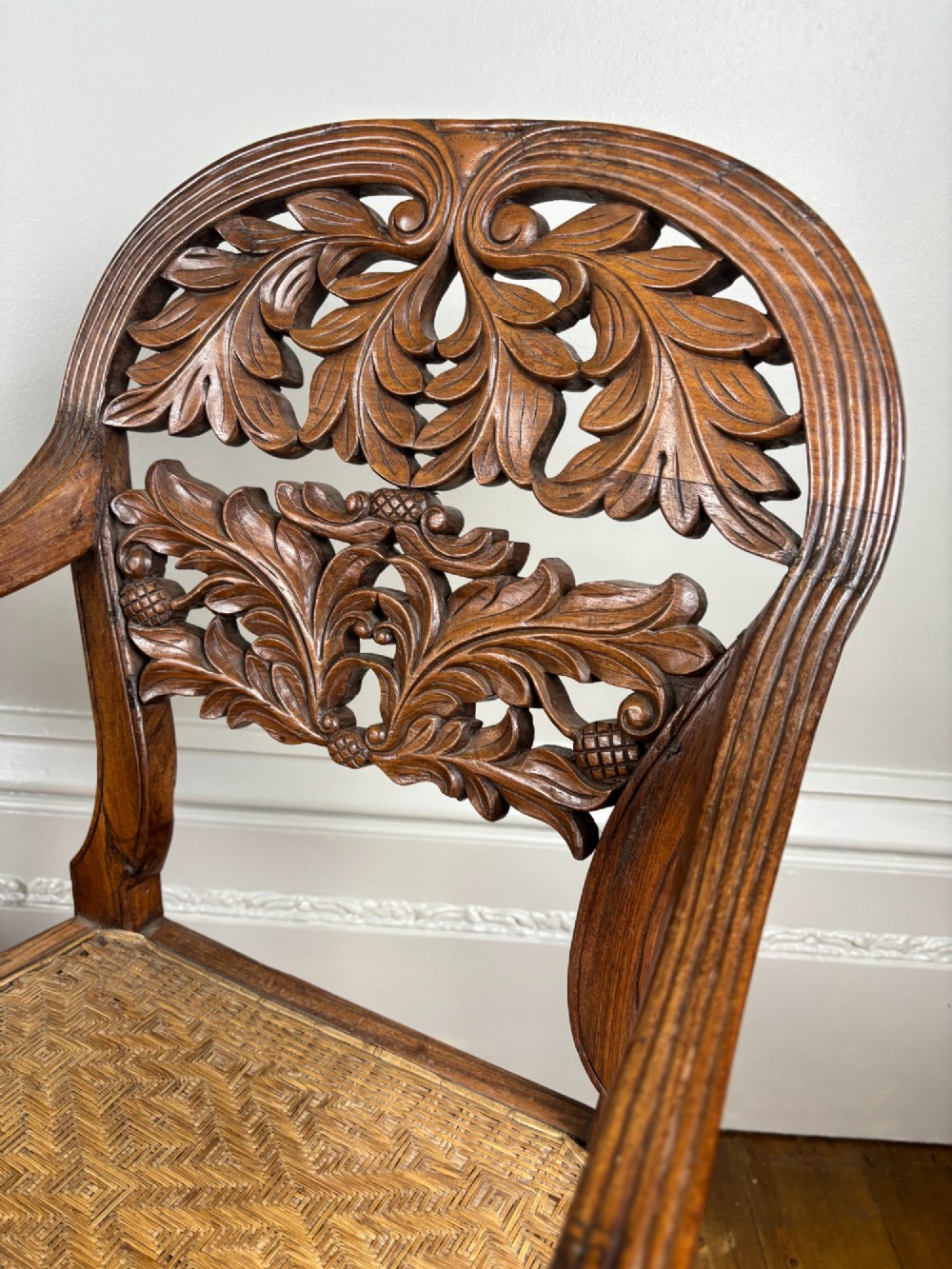 A pair of carved dark wood armchairs featuring openwork foliage backrests, curved arms, turned front legs, and woven cane seats. View III
