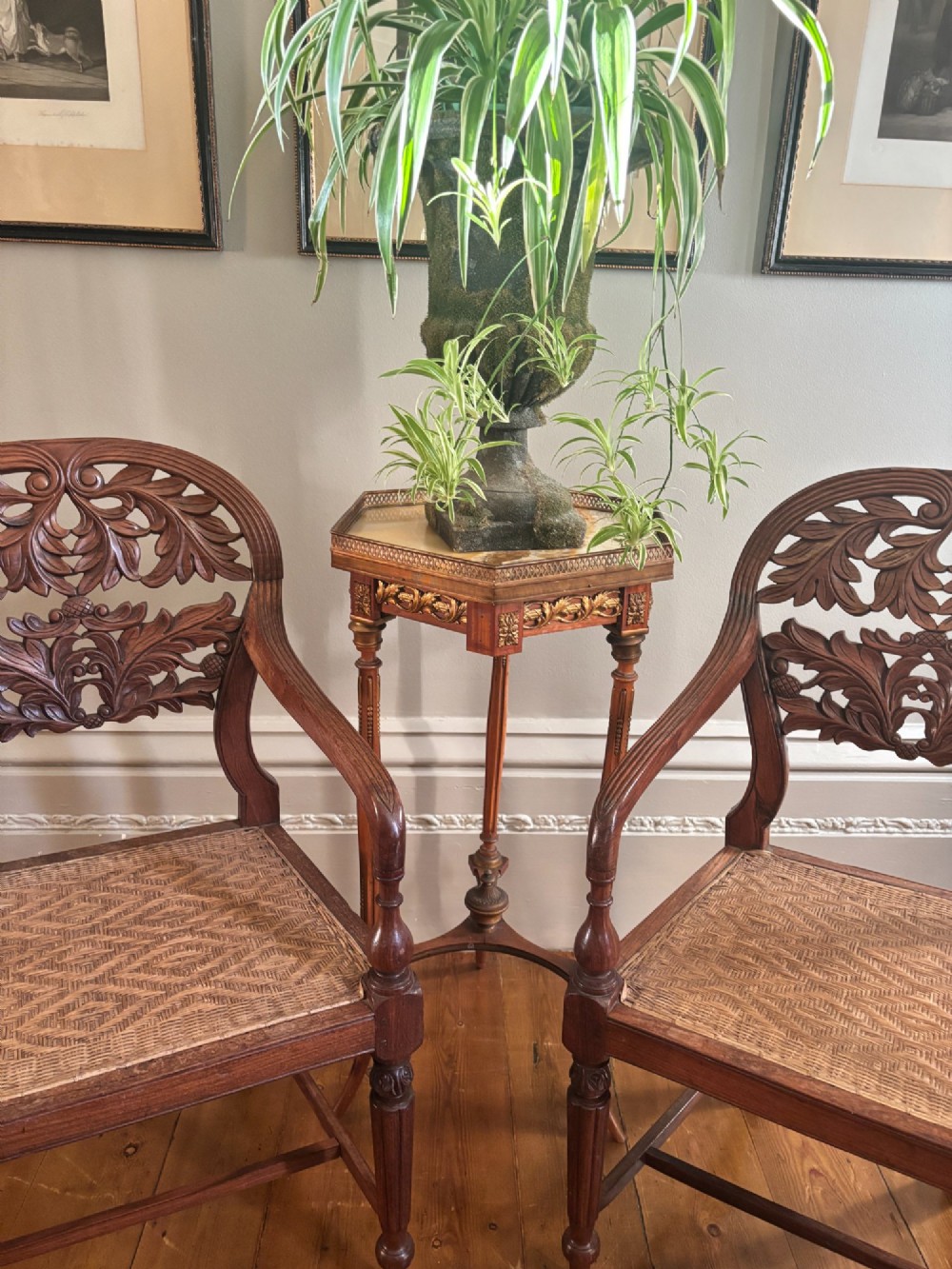 A pair of carved dark wood armchairs featuring openwork foliage backrests, curved arms, turned front legs, and woven cane seats. View IX