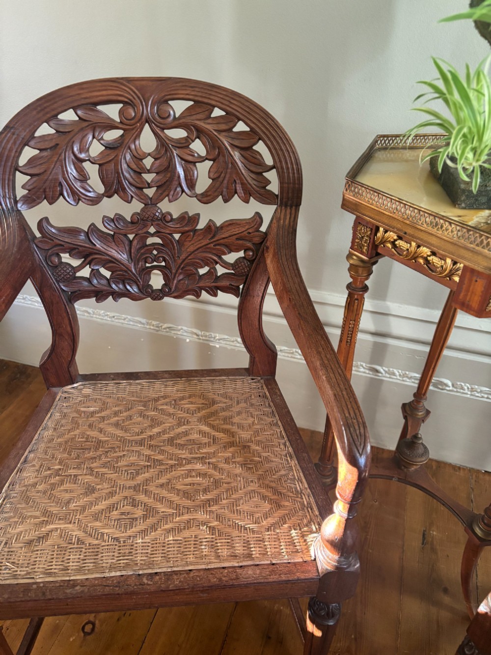 A pair of carved dark wood armchairs featuring openwork foliage backrests, curved arms, turned front legs, and woven cane seats. View X