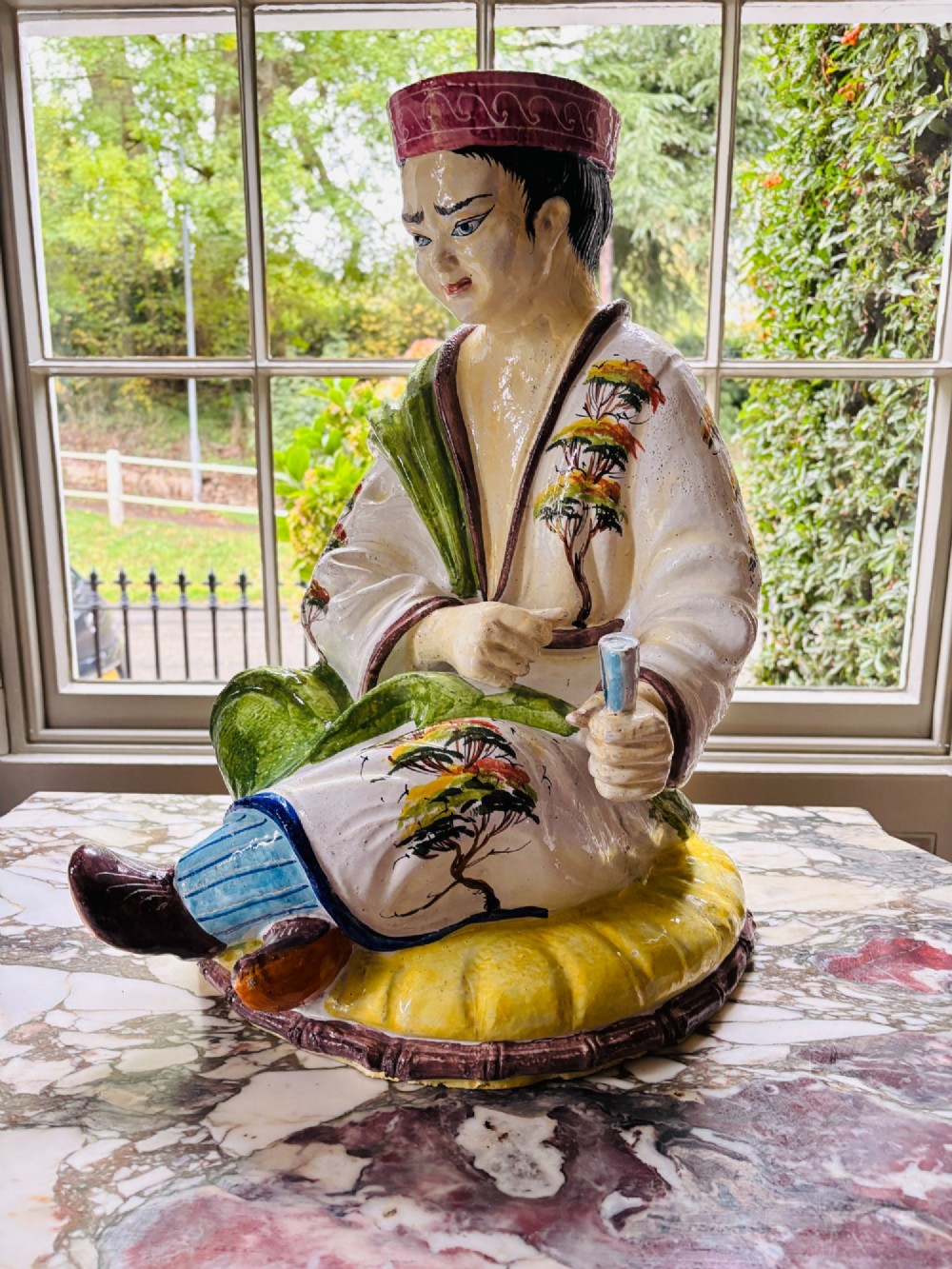 A polychrome glazed Italian ceramic figure of a seated Chinese scholar dressed in robes on a yellow cushion. View II