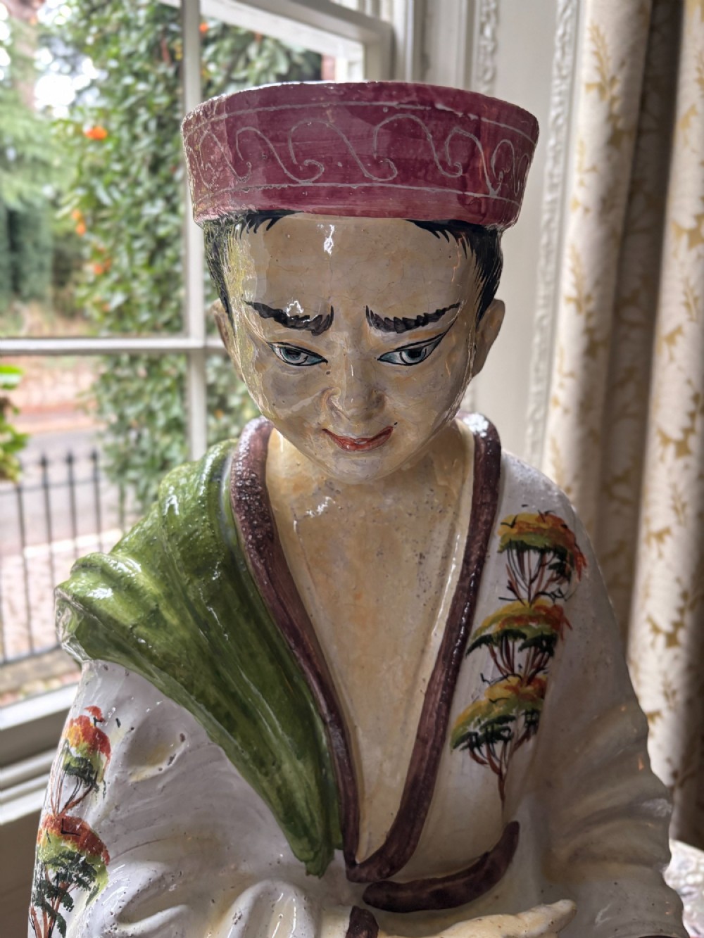 A polychrome glazed Italian ceramic figure of a seated Chinese scholar dressed in robes on a yellow cushion. View III