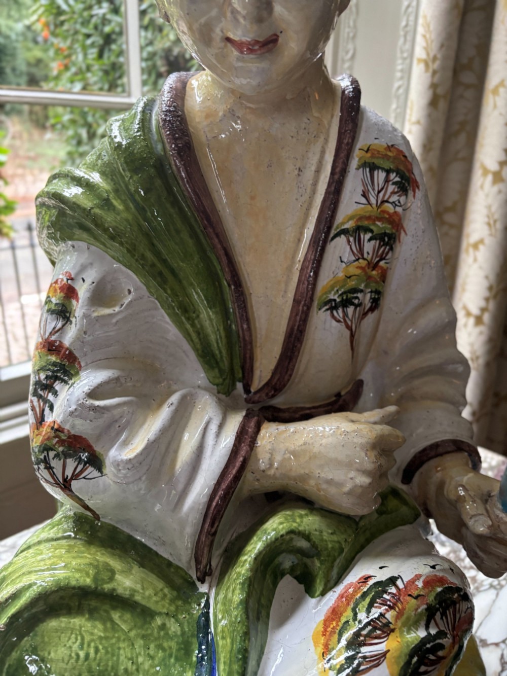 A polychrome glazed Italian ceramic figure of a seated Chinese scholar dressed in robes on a yellow cushion. View IV