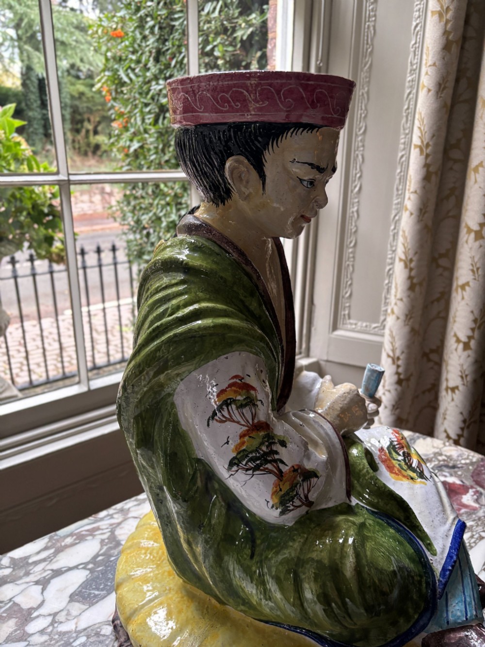 A polychrome glazed Italian ceramic figure of a seated Chinese scholar dressed in robes on a yellow cushion. View VII