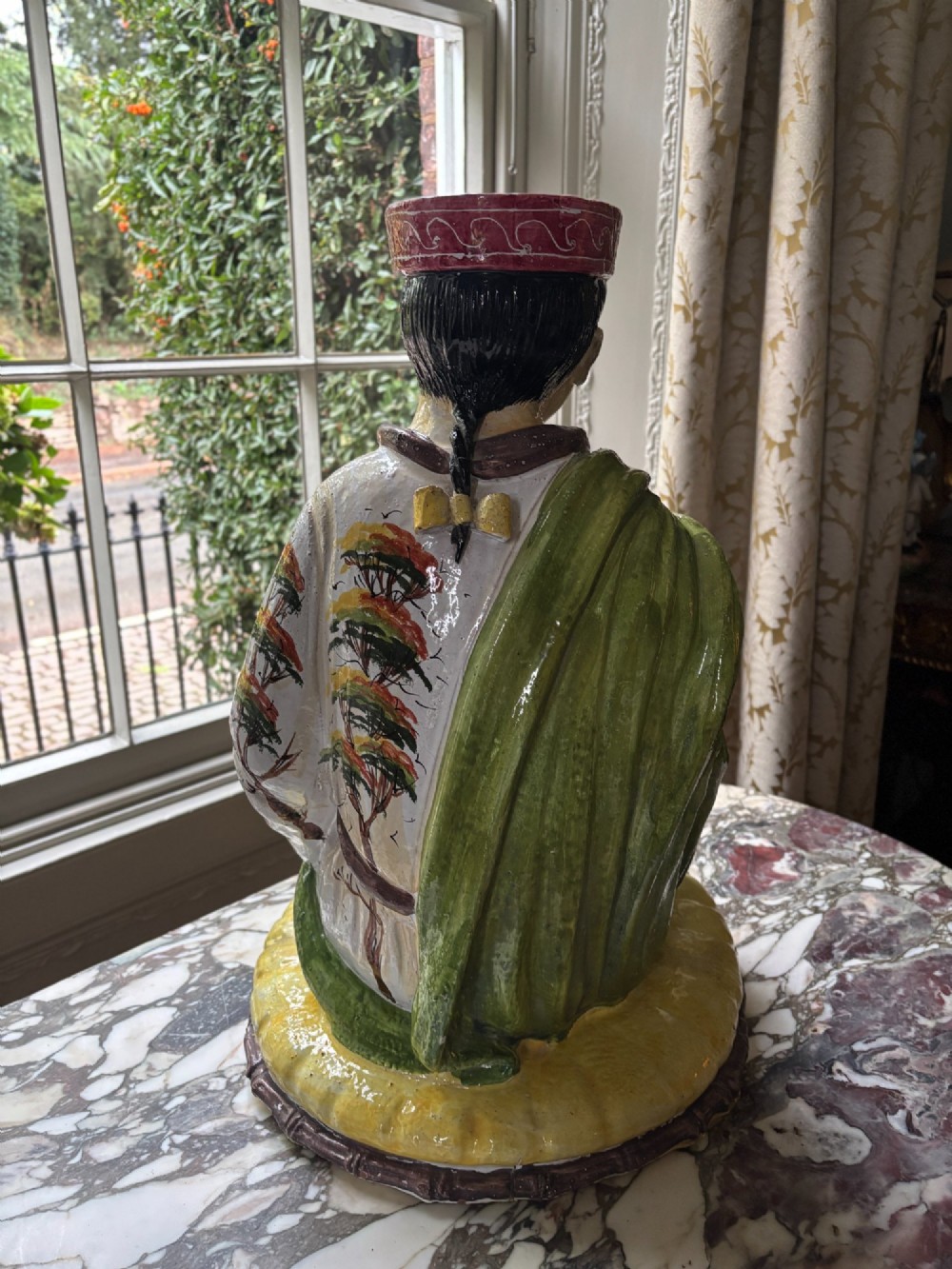 A polychrome glazed Italian ceramic figure of a seated Chinese scholar dressed in robes on a yellow cushion. View VIII