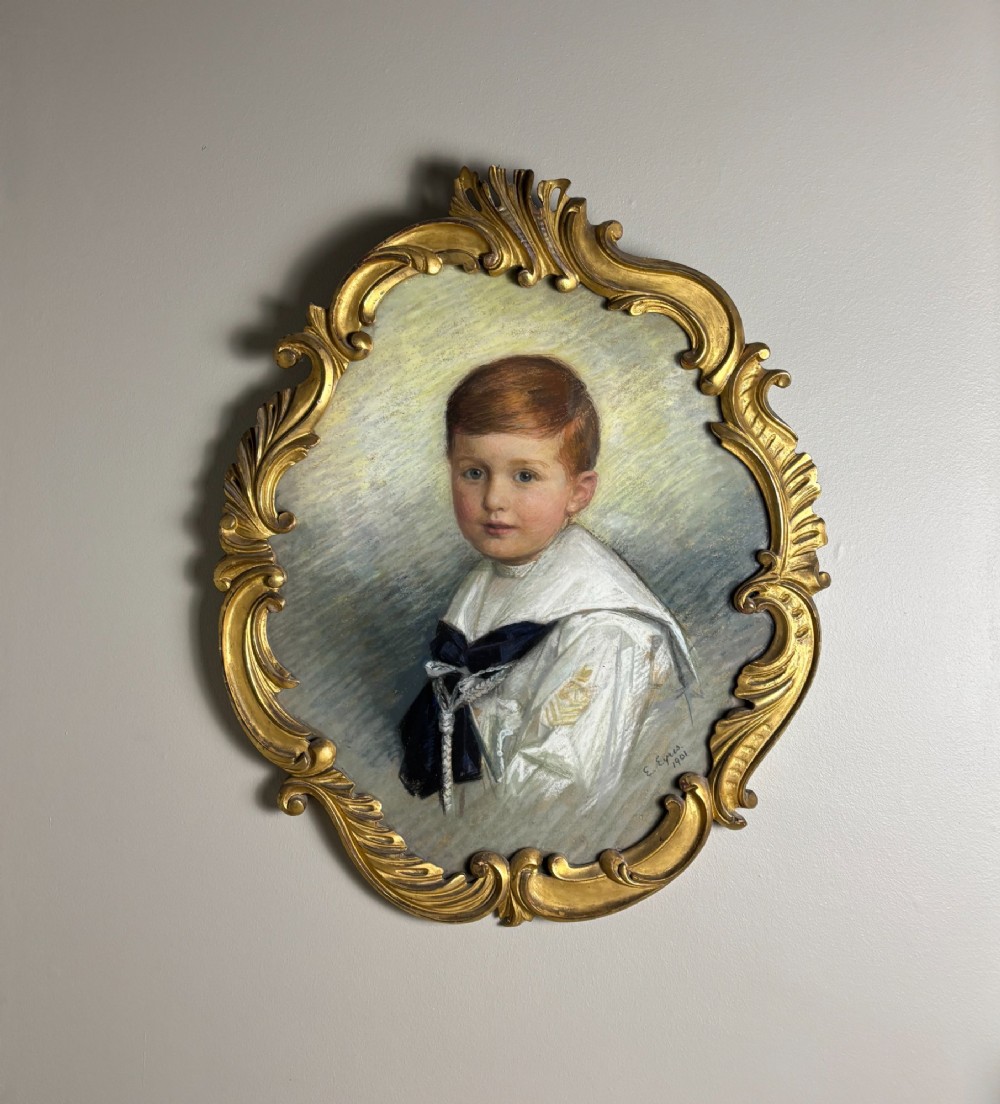 An oval Edwardian portrait of a young boy wearing a white sailor suit, set within a gilt scrollwork frame.