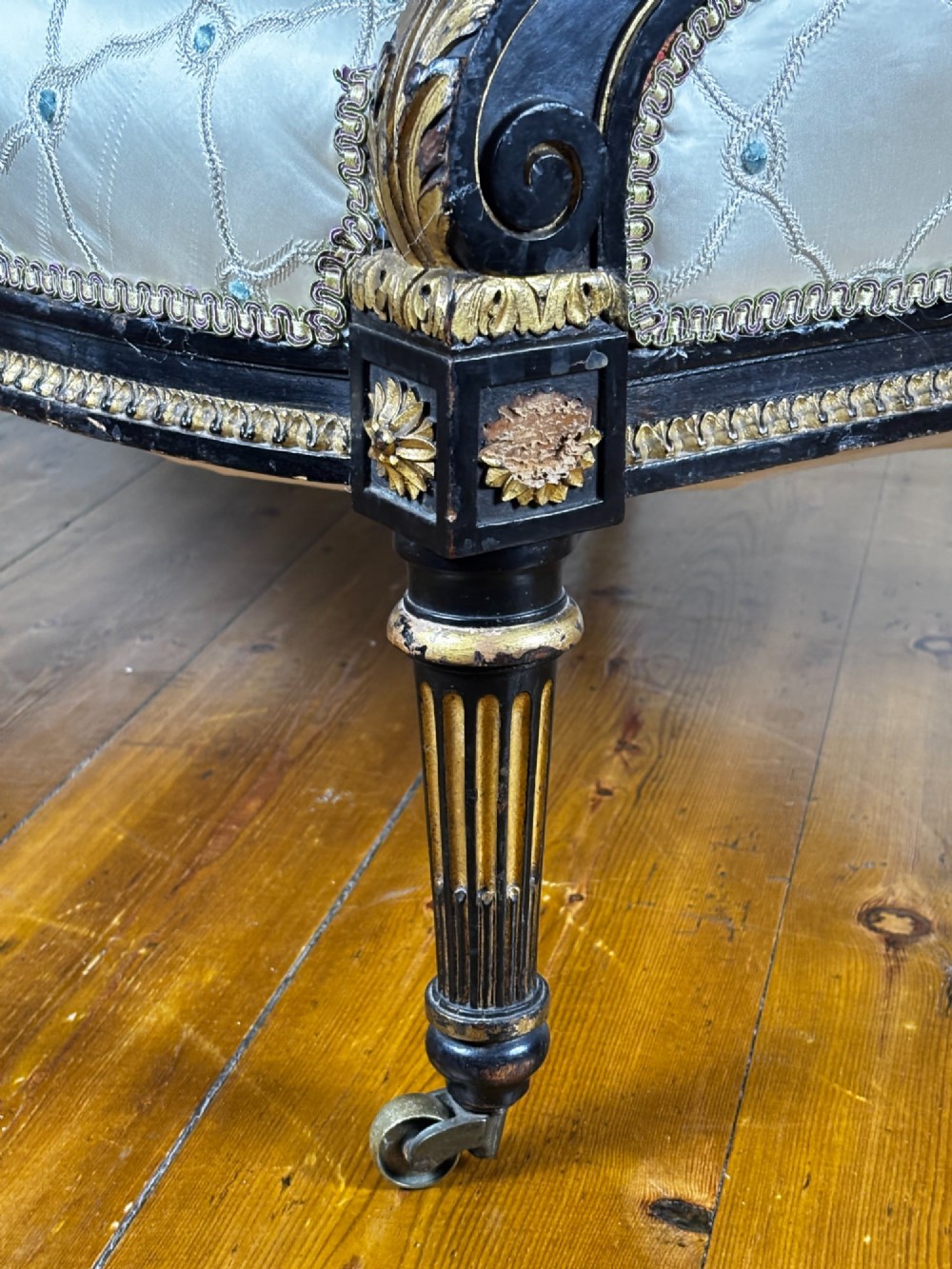 An ebonised and parcel gilt French settee featuring an oval back upholstered in floral embroidered silk, fluted legs, and brass castors. View VIII