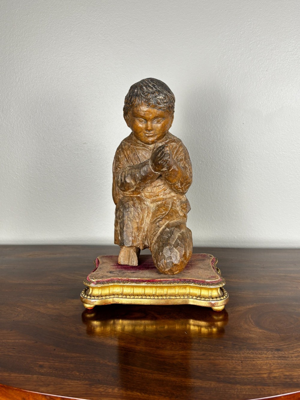 A late 18th-century carved limewood figure of a kneeling youth with hands folded in prayer, mounted on a velvet and gilded wooden base. View II