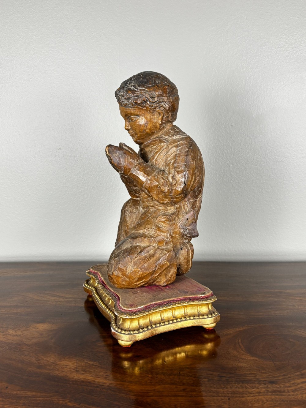 A late 18th-century carved limewood figure of a kneeling youth with hands folded in prayer, mounted on a velvet and gilded wooden base. View IV