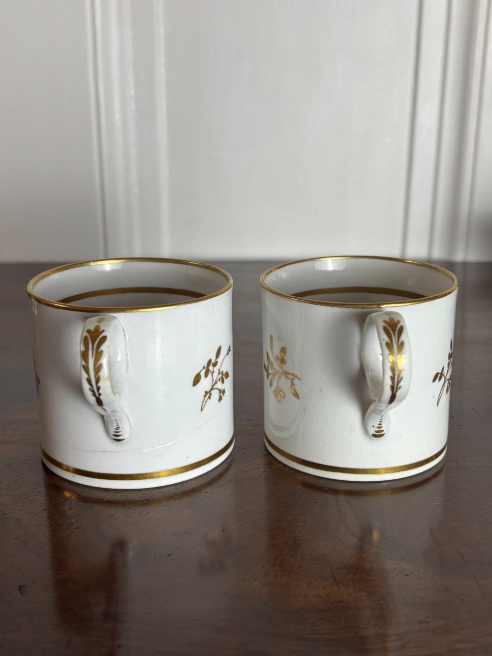A pair of cylindrical white porcelain coffee cans decorated with hand-painted landscape vignettes enclosed in ornate gilded oval frames. View VI