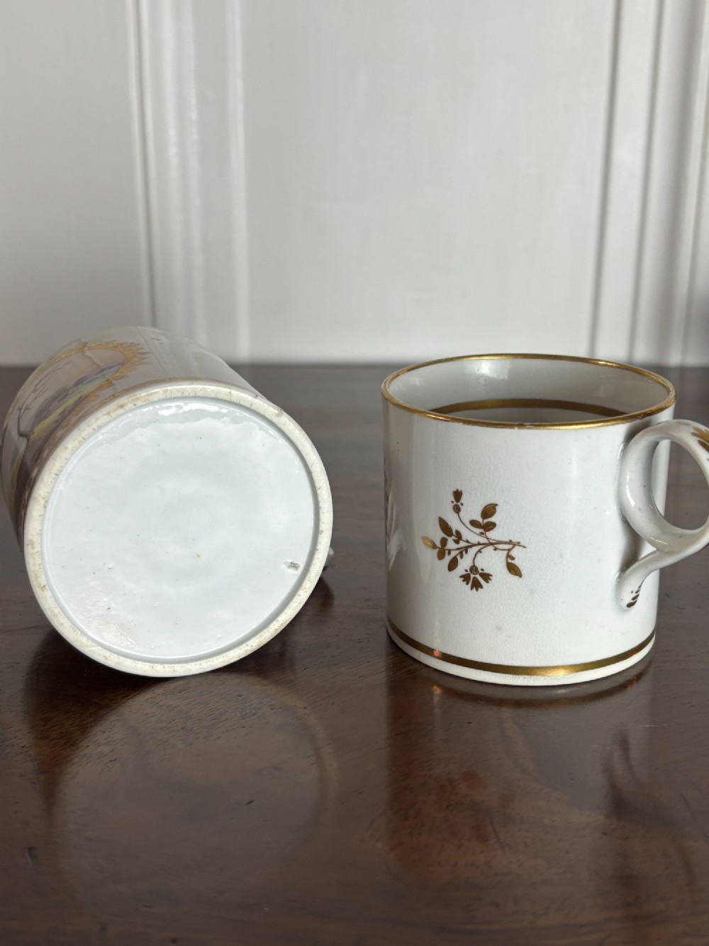 A pair of cylindrical white porcelain coffee cans decorated with hand-painted landscape vignettes enclosed in ornate gilded oval frames. View VII