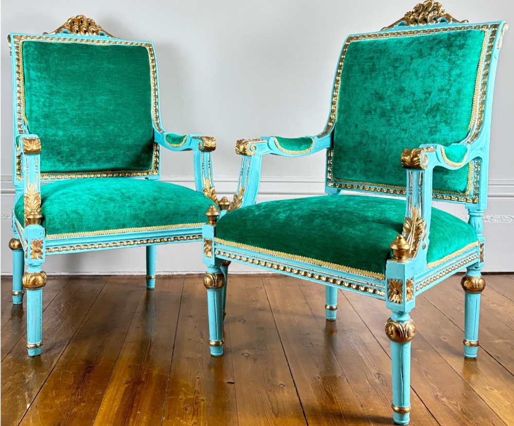 A pair of 19th-century French open armchairs featuring carved turquoise painted frames with gold gilt accents and emerald green velvet upholstery.
