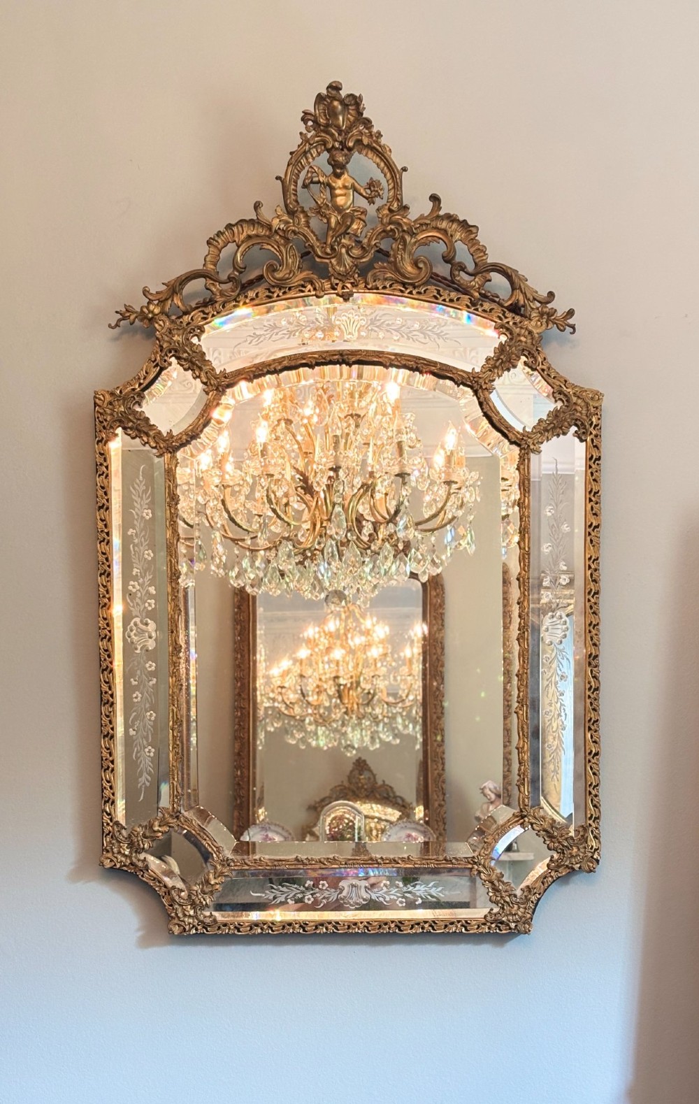 An ornate French Louis XV style gilt bronze wall mirror featuring etched glass borders, C-scroll framework, and a cherub cresting. View II