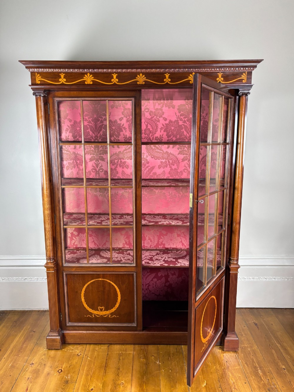A tall Georgian rosewood display cabinet featuring two glazed doors lined with red damask fabric, flanked by columns and adorned with marquetry inlays. View X