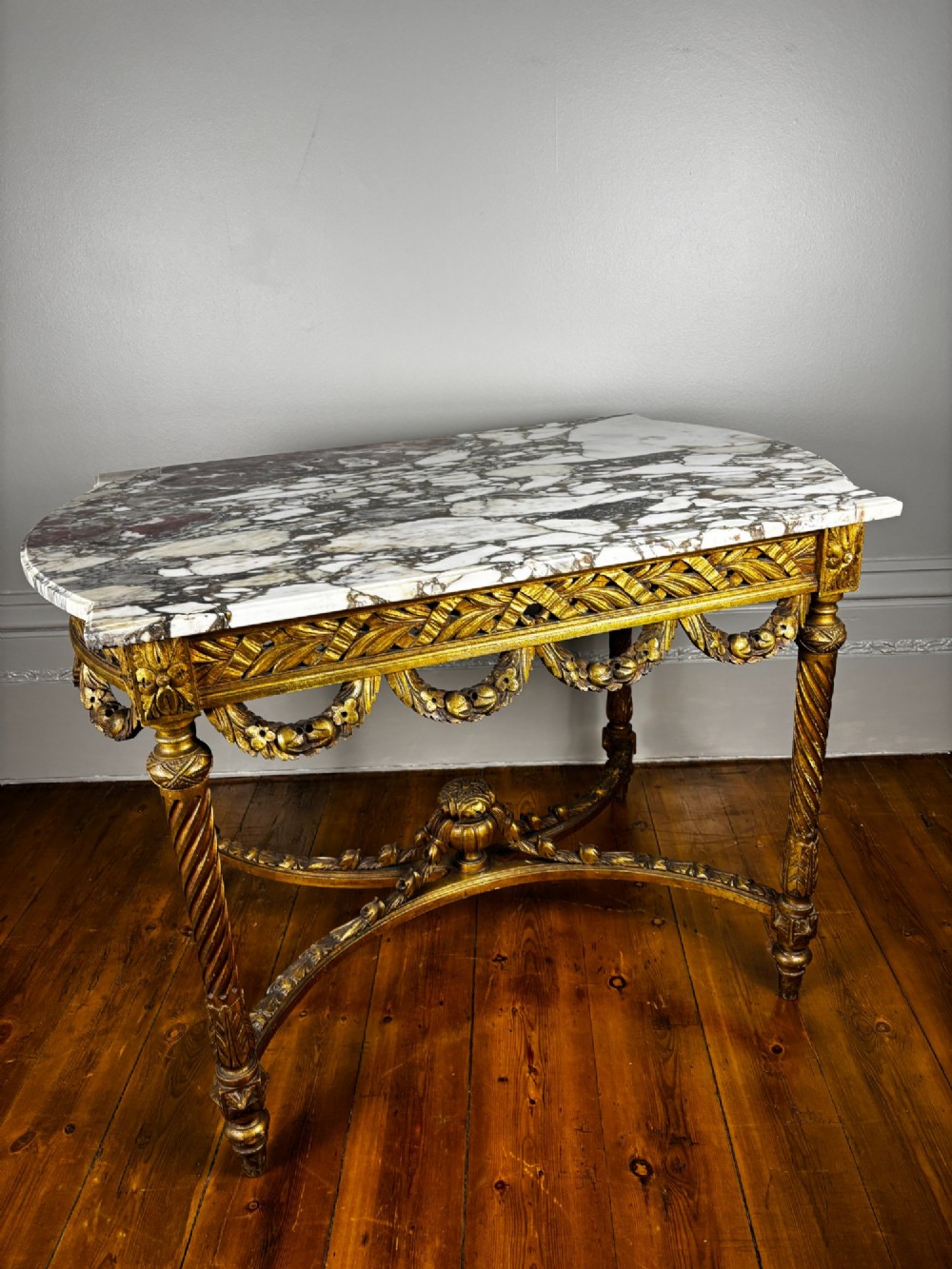 An antique French revival side table featuring a white carved marble top, a carved gold gilt frame with drapery swags, spiral-fluted legs, and a central cross stretcher. View III