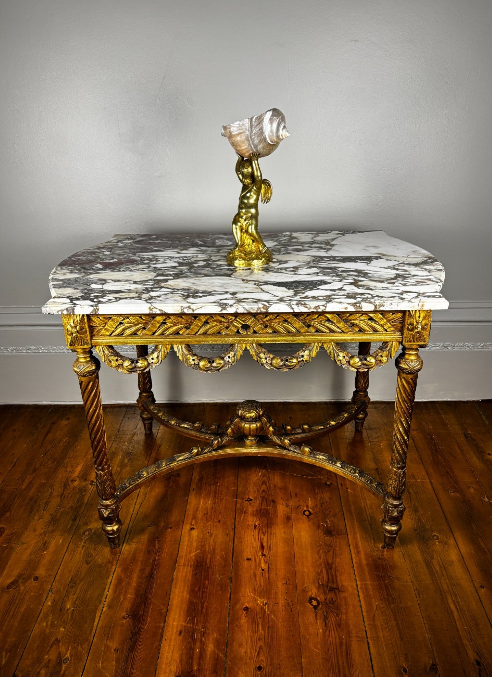 An antique French revival side table featuring a white carved marble top, a carved gold gilt frame with drapery swags, spiral-fluted legs, and a central cross stretcher. View IX