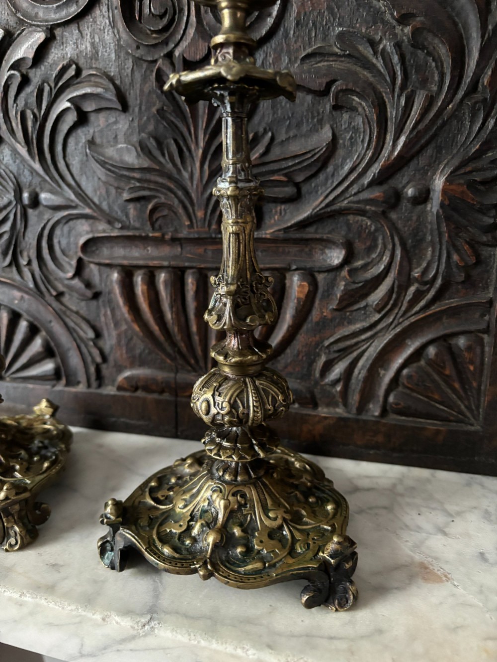 A pair of ornate 19th-century Regency brass candlesticks featuring detailed relief moulding and scrollwork bases holding lit candles. View III