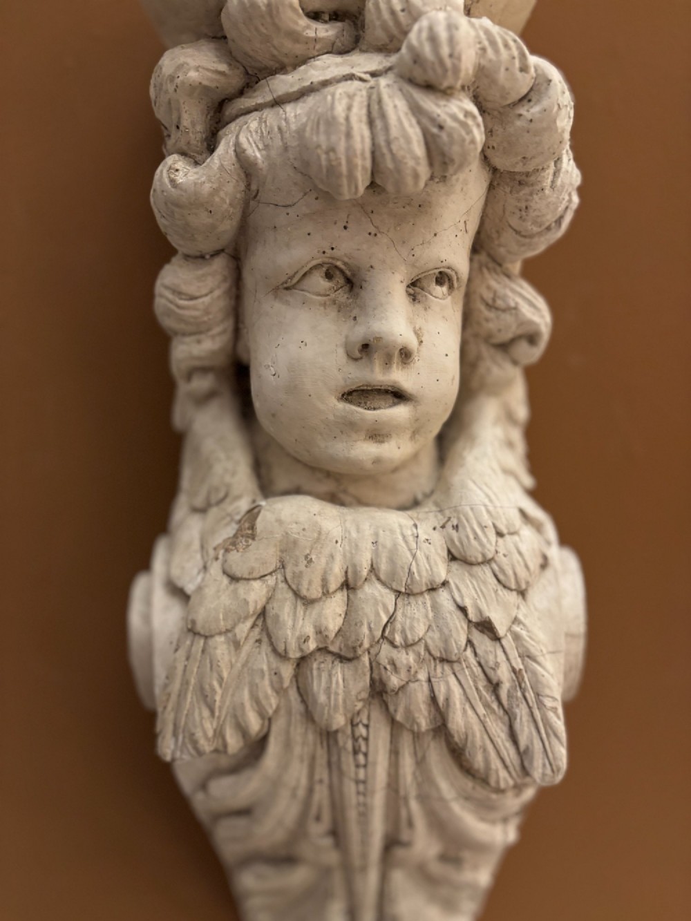 A 19th-century carved off-white architectural wall corbel featuring a winged putto head above acanthus leaf details. View X
