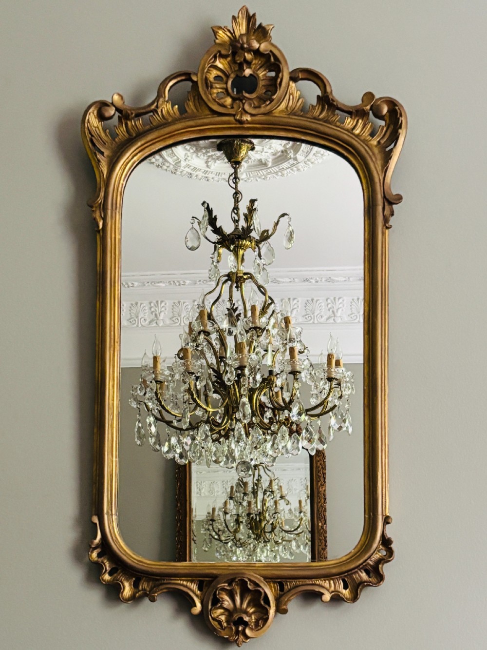 A tall French giltwood pier mirror featuring an ornate carved shell motif crest, decorative scrollwork frame, and gold leaf finish.