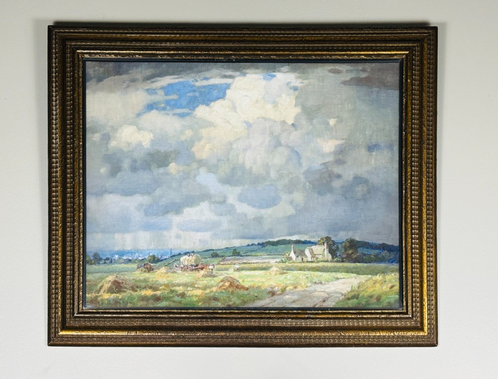 An Edwardian oil painting on board depicting a rural landscape with haystacks, cottages, and clouds set within a moulded frame. View VII