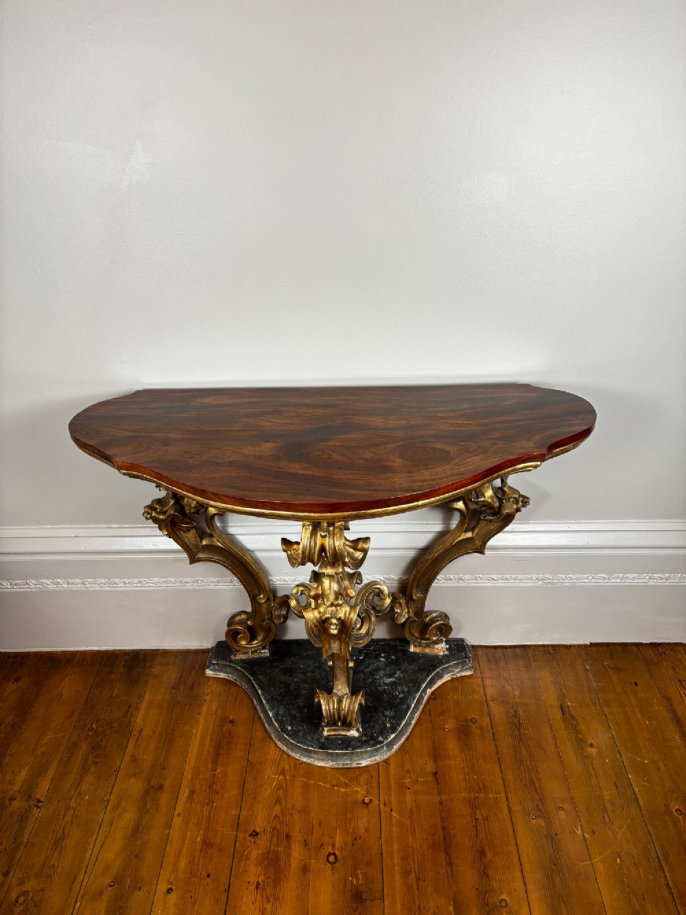 An 18th-century Venetian console table featuring intricate carved giltwood legs with scroll motifs resting on a shaped dark base beneath a polished dark timber top. View II