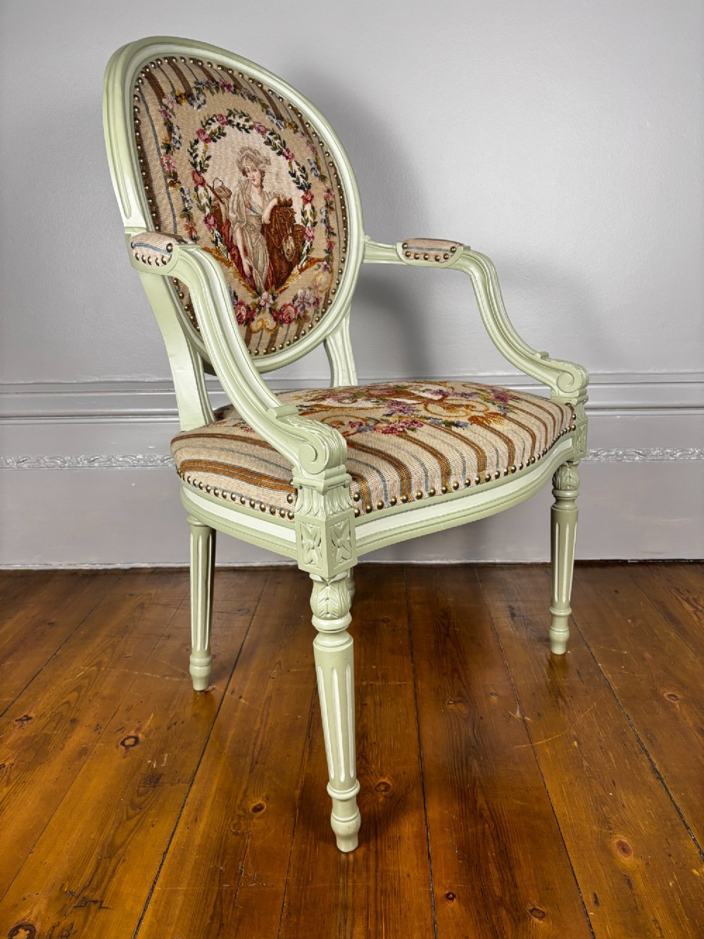 An 18th-century style pale green painted open armchair featuring an oval backrest and seat upholstered in petit point tapestry depicting floral and figural motifs. View IV
