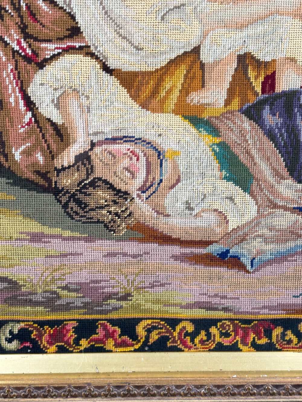 A Victorian Berlin needlepoint embroidery depicting a mother seated with two children inside an arched border and heavily carved giltwood frame. View III